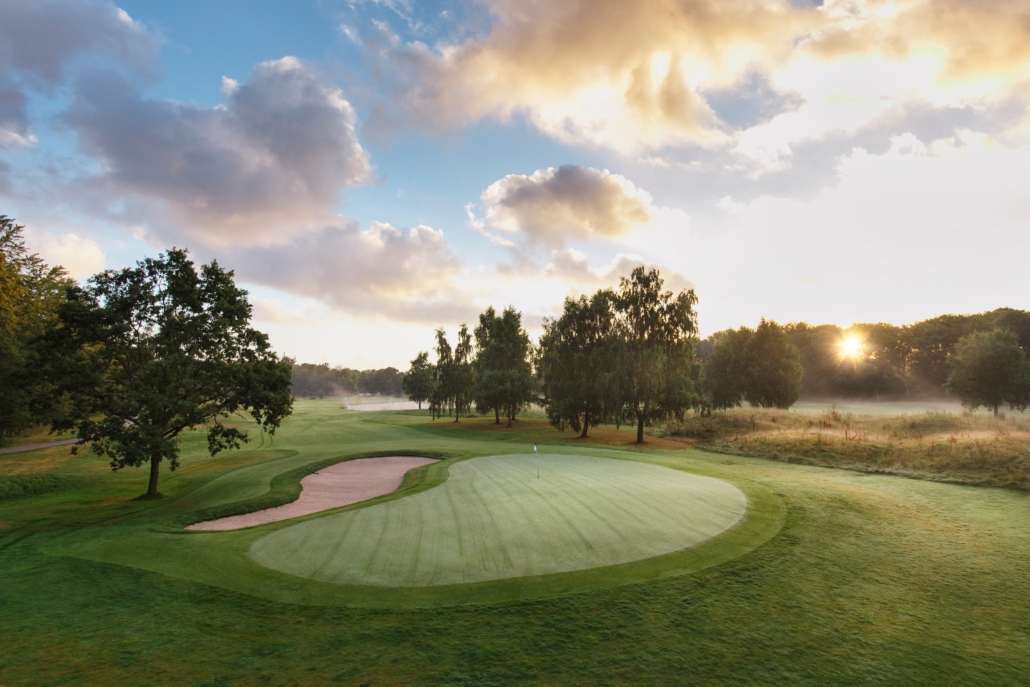 A golf course with a green field and trees

Description automatically generated